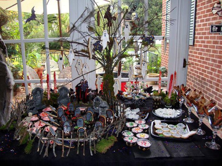 Creepy Halloween dessert table decor with ghosts hanging from a tree and a graveyard centerpiece