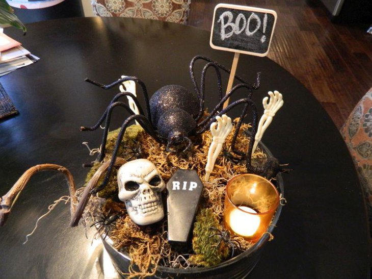 Scary DIY Halloween table centerpiece with a black bucket filled with dry grass skull spider and sipper with candle