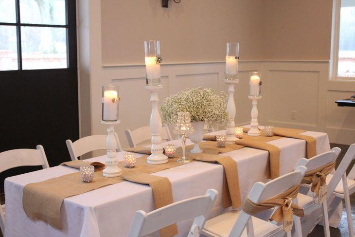 Scented white candles on wooden stands as dining table centerpieces