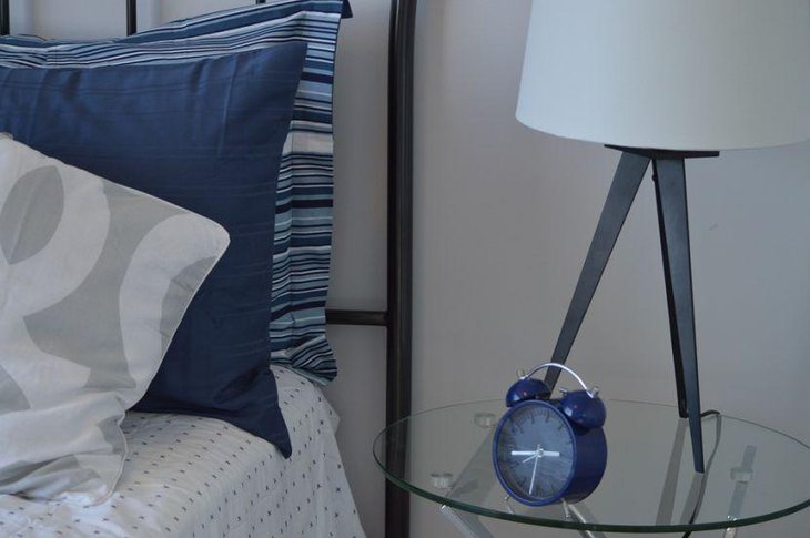A blue alarm clock lends a serene touch to this glass bedside table