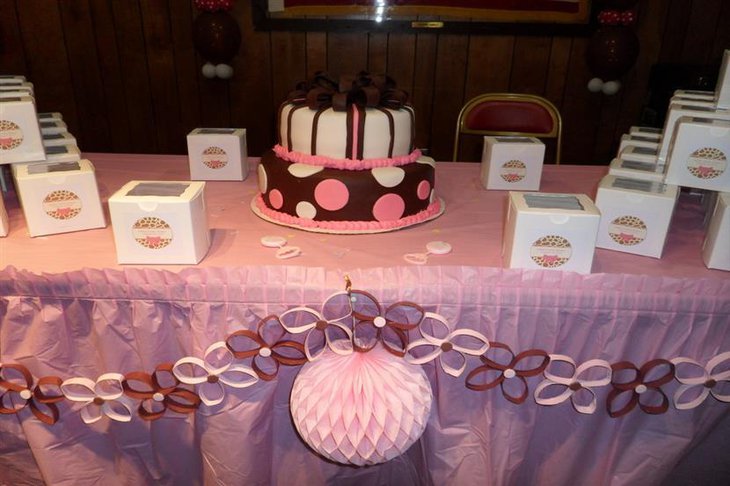 A pink baby shower cake for a baby girl accentuated with brown ribbons