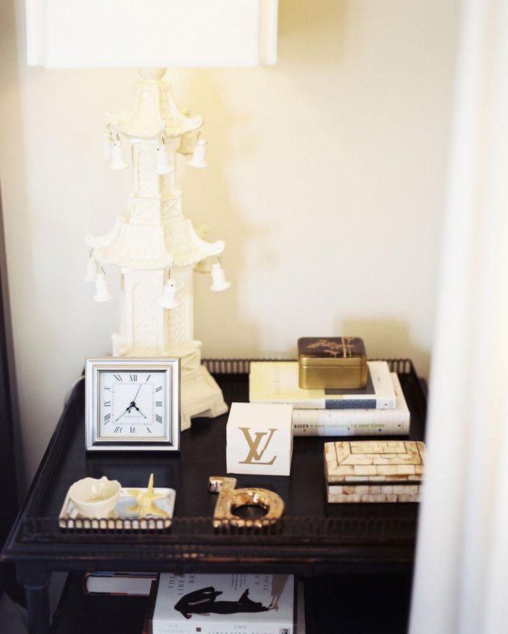 A wooden bedside table decorated with a clock and decorative lamp