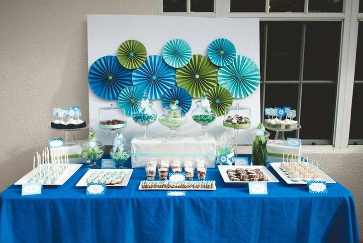 Boy baby shower dessert table idea with blue pinwheels tablecloth and cupcake sticks