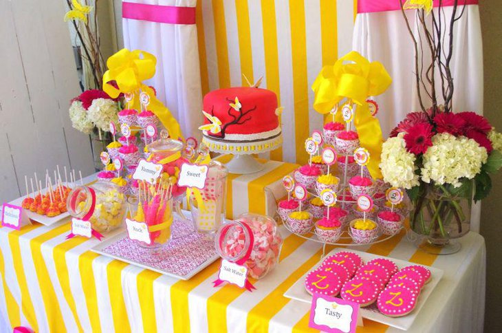 Bright yellow and pink accented wedding cake table decorations with cupcakes and candies