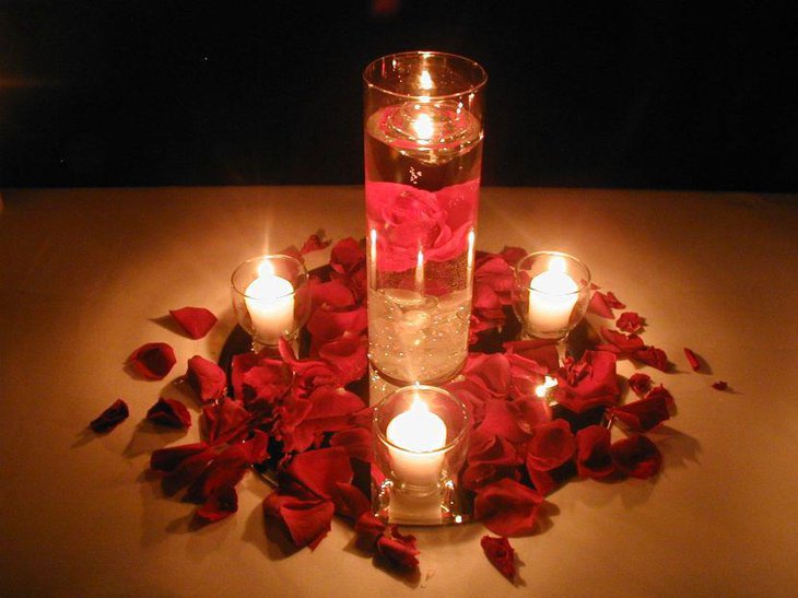 Candles decorated in glass with red rose petals as table centerpiece for weddings