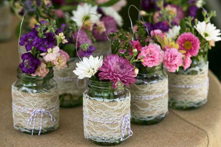 Colorful flowers presented in mason jars adorned with lace and colored strings