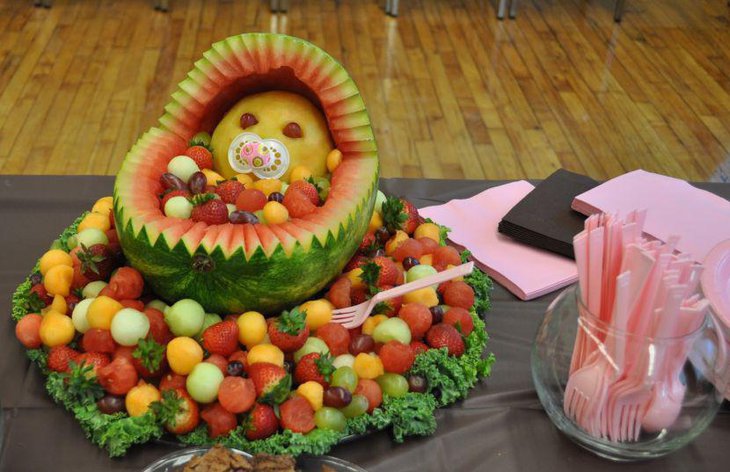 Cute baby crib carved out of watermelon sitting on a delicious fruit platter