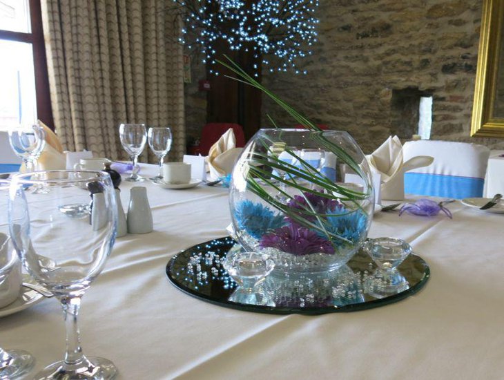 Gorgeous fish bowl and mirror with colourful flowers as dining table centerpiece