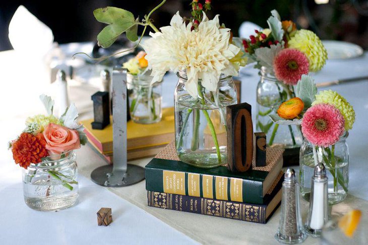 Interesting DIY centerpiece with glass jars books and fresh flowers