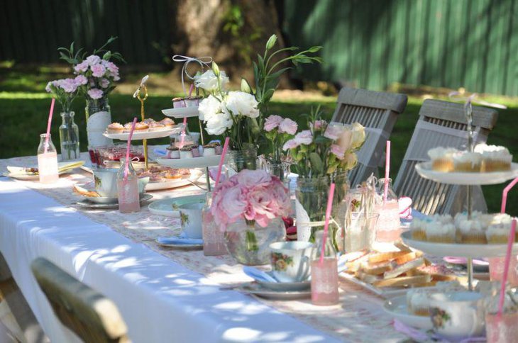 Subtle white and pink themed summer garden party table decoration with flowers and leaves in glass jars