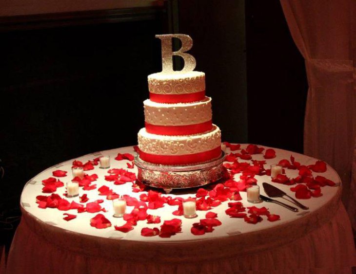 Three tiered wedding cake decor with red ribbons and petals