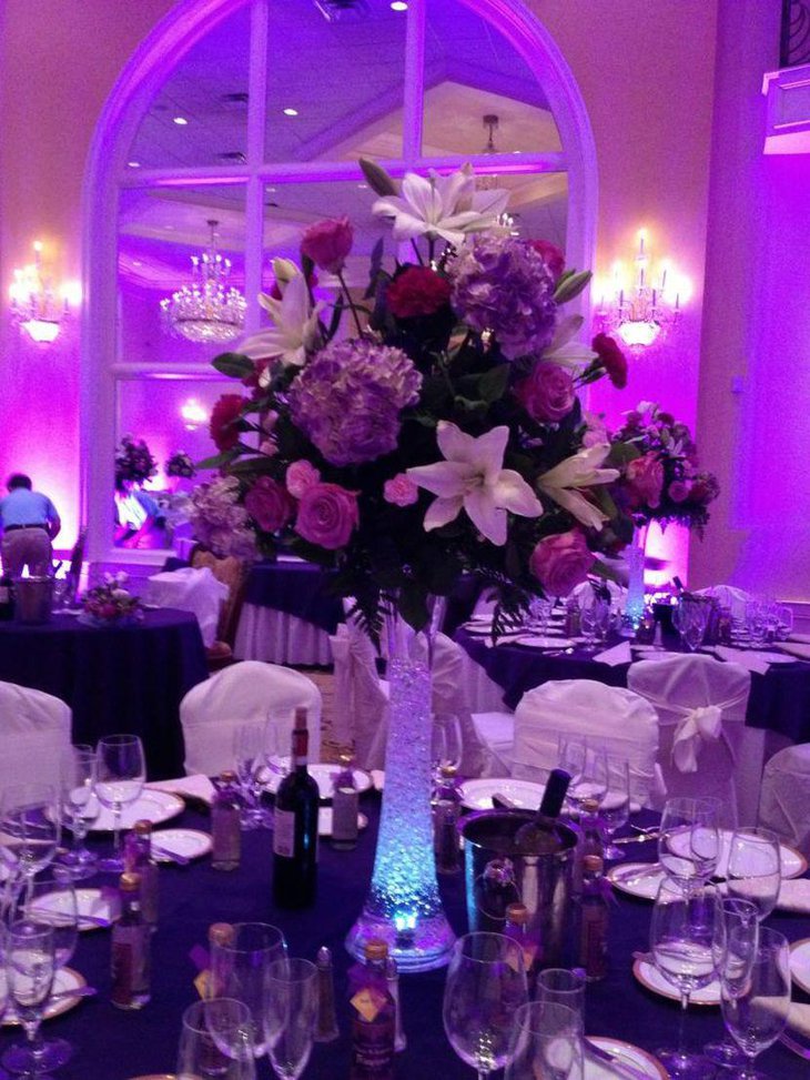 Wedding table decor featuring tall glass vase with purple accented flowers