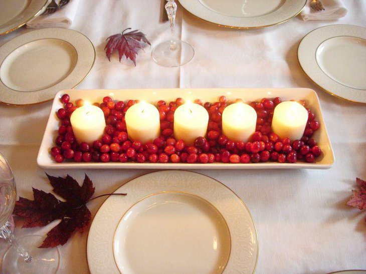 White candles in white tray filled with red berries for wedding centerpiece