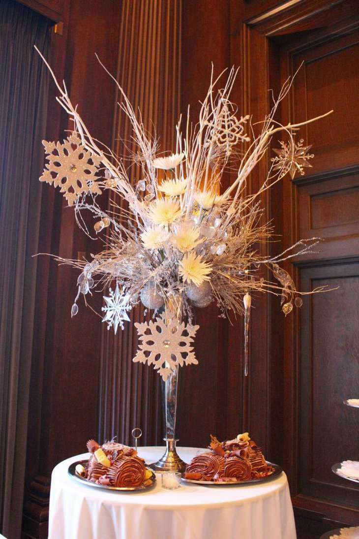 Winter table setting with tall vase fillwed with branches flowers and hanging snowflakes